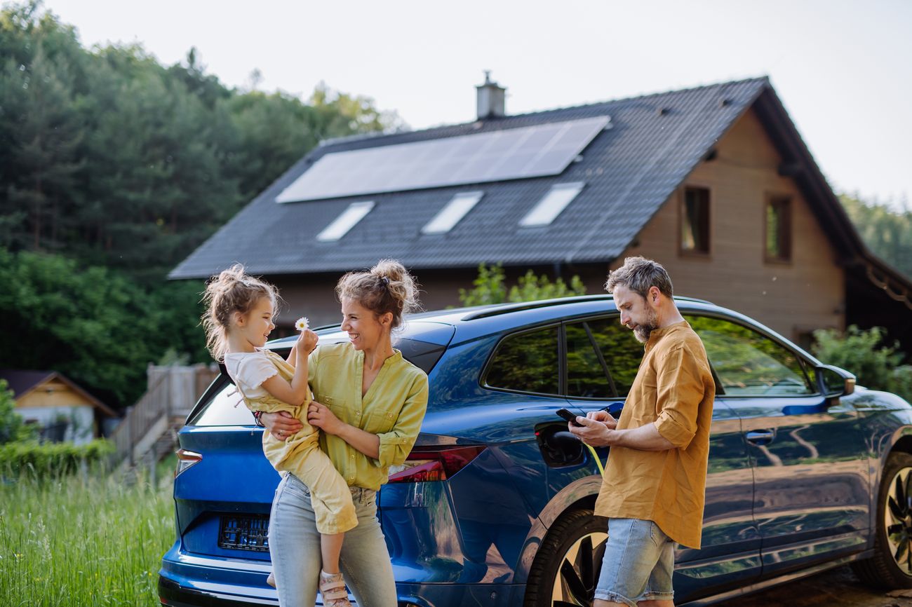 配有太阳能板的住宅与混合动力汽车旁的一家人